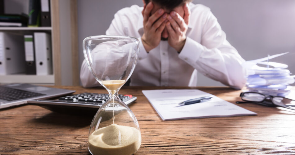 Close-up Of A Hourglass In Front Of Upset Businessman In Office