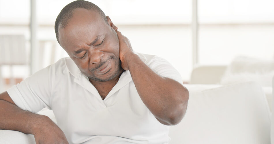 Elderly african man suffering from neck pain at home on couch. Males sense of fatigue, exhausted, stressed. African man massages her painful neck with her hands. The concept of body and health.