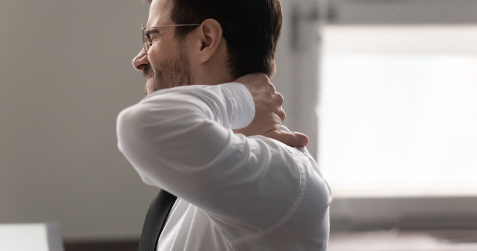 Close up unhappy businessman massaging neck, suffering from pain. Male employee massaging stiff neck muscles after sedentary computer work in incorrect posture or uncomfortable chair at workplace.