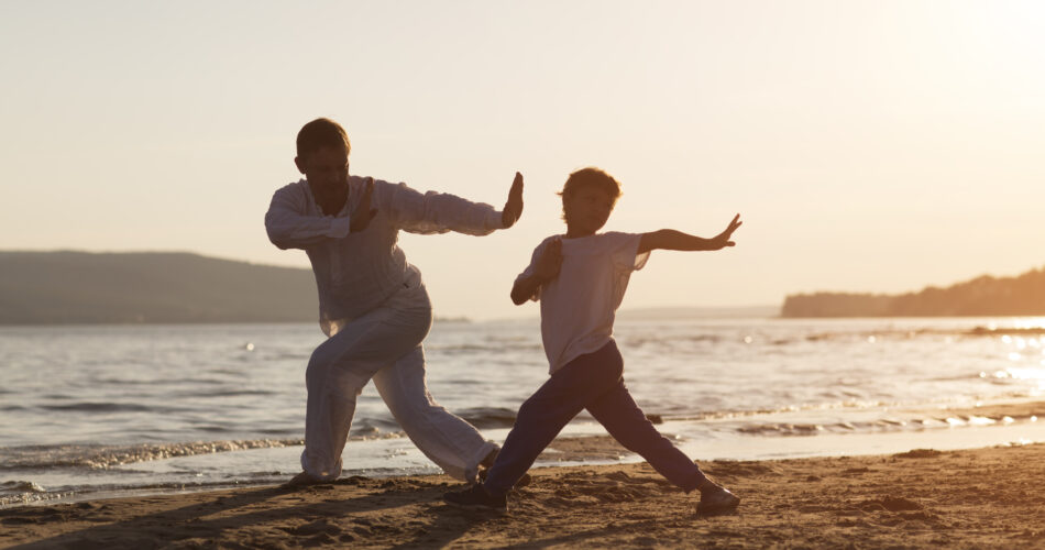 Pai de família e filho pré-escolar praticam Tai Chi Chuan no verão na praia.  habilidade de gestão chinesa Qi's energia. atividades ao ar livre solo. Distância social. exercício familiar em conjunto.