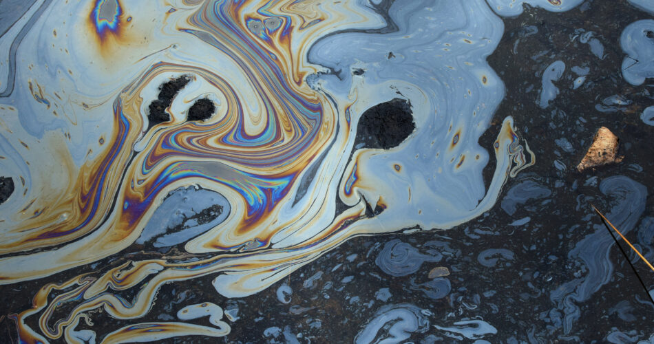 Iridescent colors abstract shapes on tar water surface of natural asphalt pit.