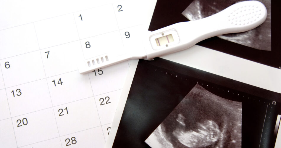 Positive white plastic pregnancy test and  calendar with ultrasound of baby in pregnant woman at three month.