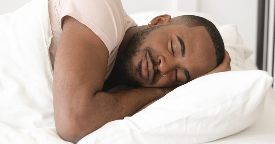 Serene calm handsome young black man sleeping well alone on orthopedic soft pillow under warm duvet, african american guy lying asleep in comfortable cozy bed enjoy good night peaceful healthy sleep