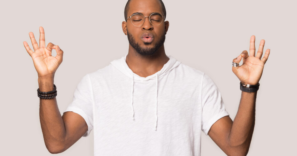 Stressed black guy meditating pose isolated on beige studio background, mixed race man in glasses folded fingers mudra symbol exhales and calms down breathing deep, self control, stress relief concept