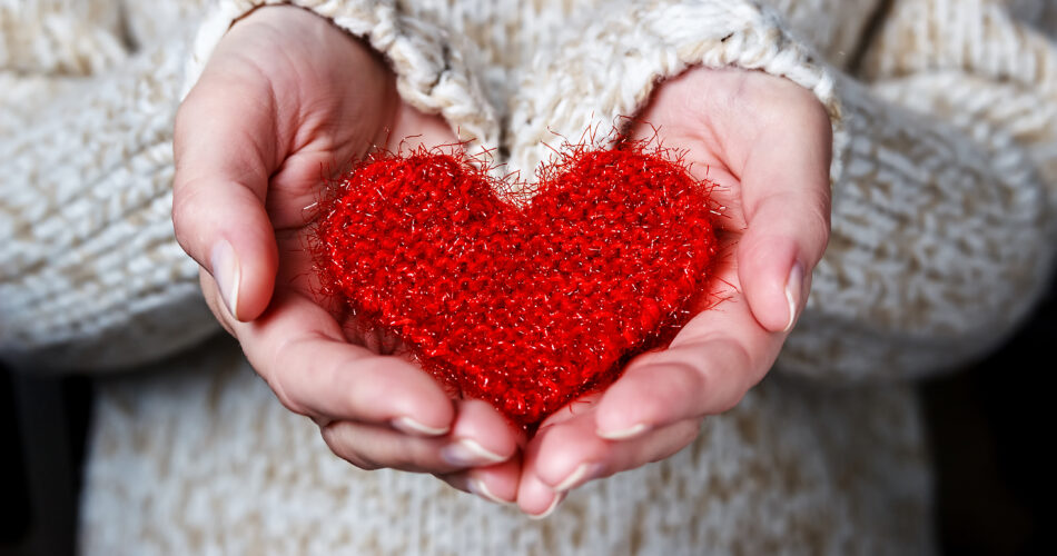 Une jeune fille dans un pull léger donne un cœur tricoté. Gros plan sur